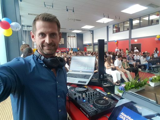 DJ vor Publikum in einem festlich dekorierten Raum, Mischpult und Laptop sichtbar.