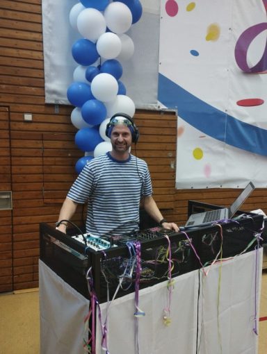 DJ steht an einem Mischpult mit Ballon-Dekoration im Hintergrund.